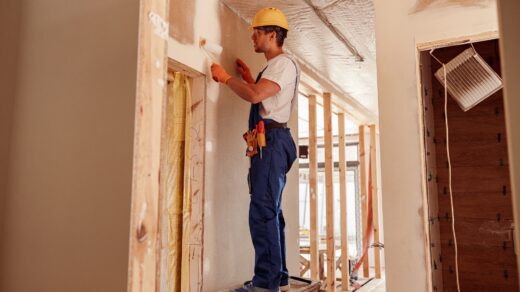 Male builder painting wall in house under construction