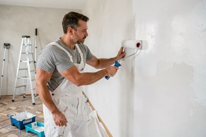 Peintre professionnel appliquant de la peinture blanche au rouleau sur un mur intérieur lors d'un chantier de rénovation